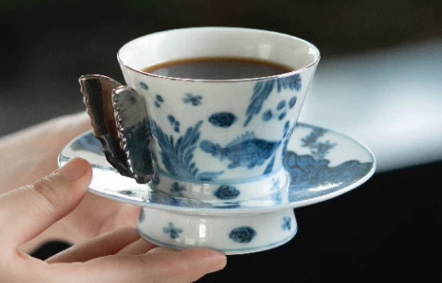 Hand holding blue and white porcelain butterfly coffee cup with dark background