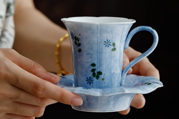 Hand-painted porcelain coffee cup and petal saucer held in hands